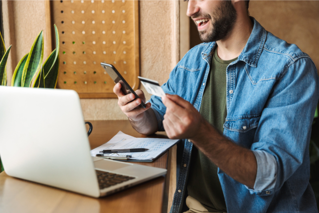 Man Using a Laptop and Holding a Smartphone Credit Card